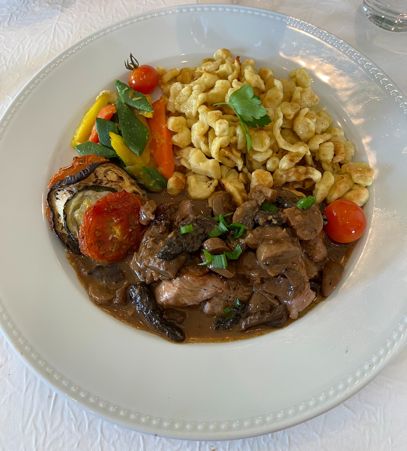 Assiette de quasi de veau en sauce brune, spatzles et légumes colorés, garnie de persil. servi au restaurant le cheval blanc