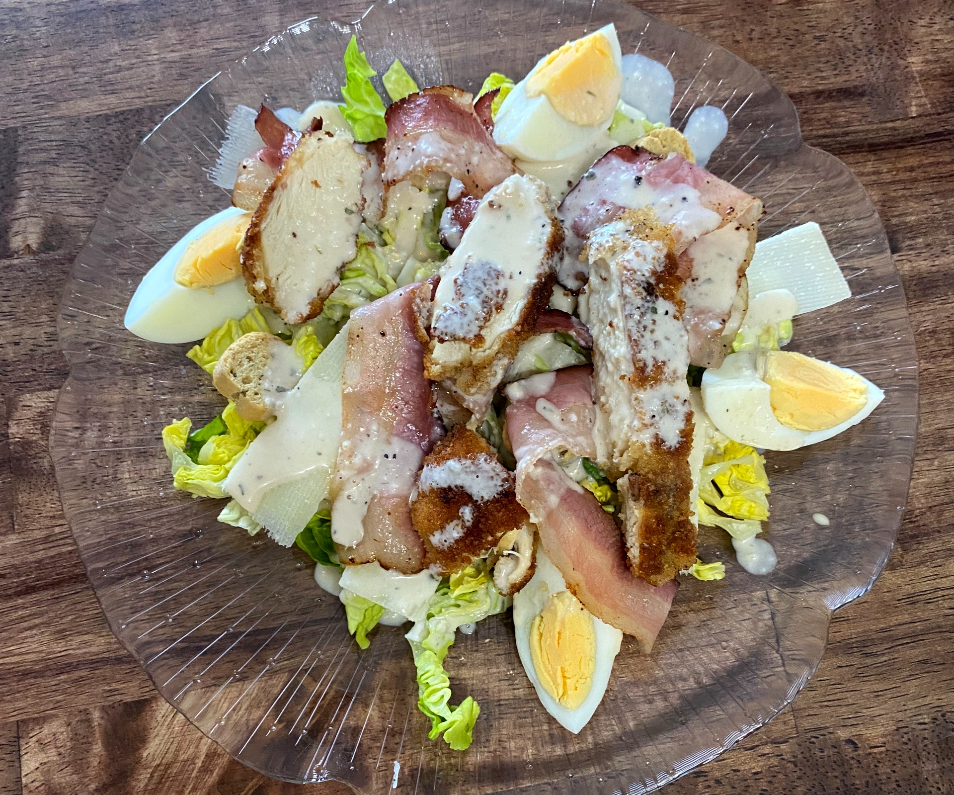 Salade verte avec œufs durs, lardons croustillants, copeaux de fromage et sauce blanche sur assiette transparente. salade césa