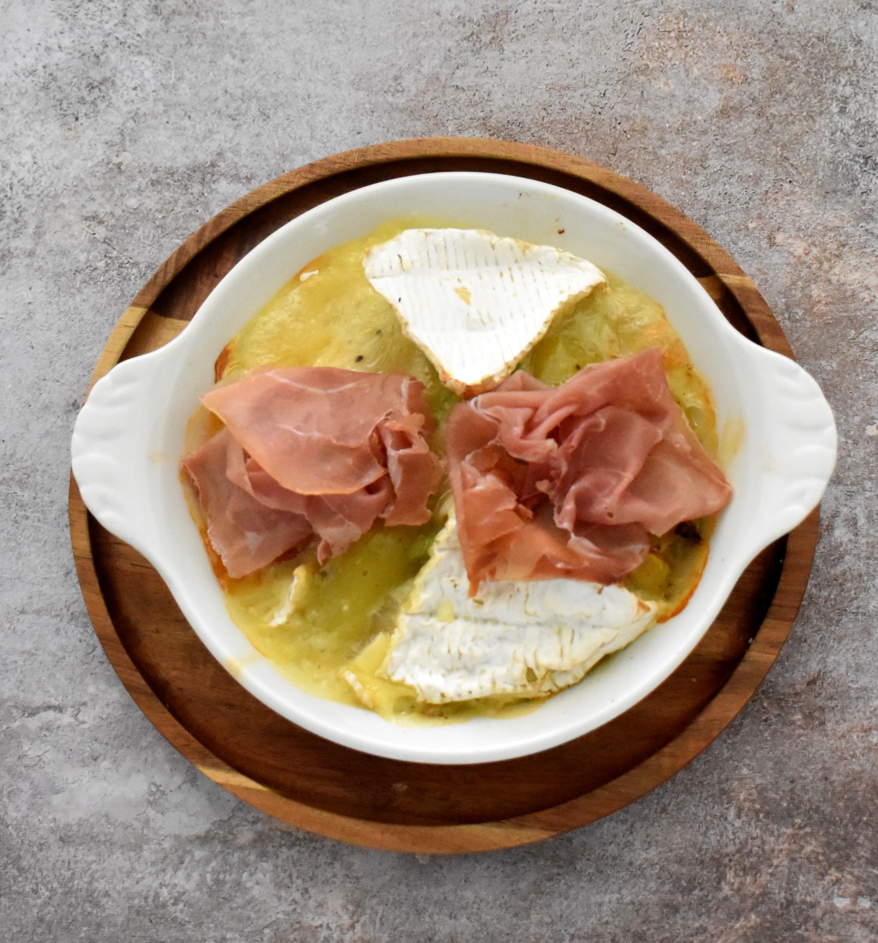 Assiette blanche sur plateau en bois, camembert fondu avec jambon cru