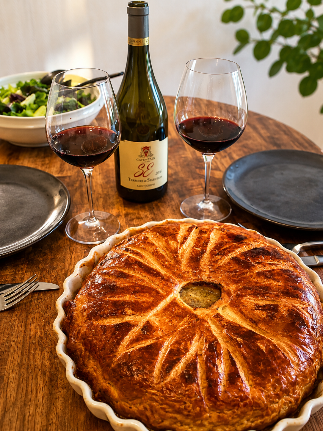 Bouteille de vin rouge, deux verres et tourte a la viande au centre d’une table en bois.