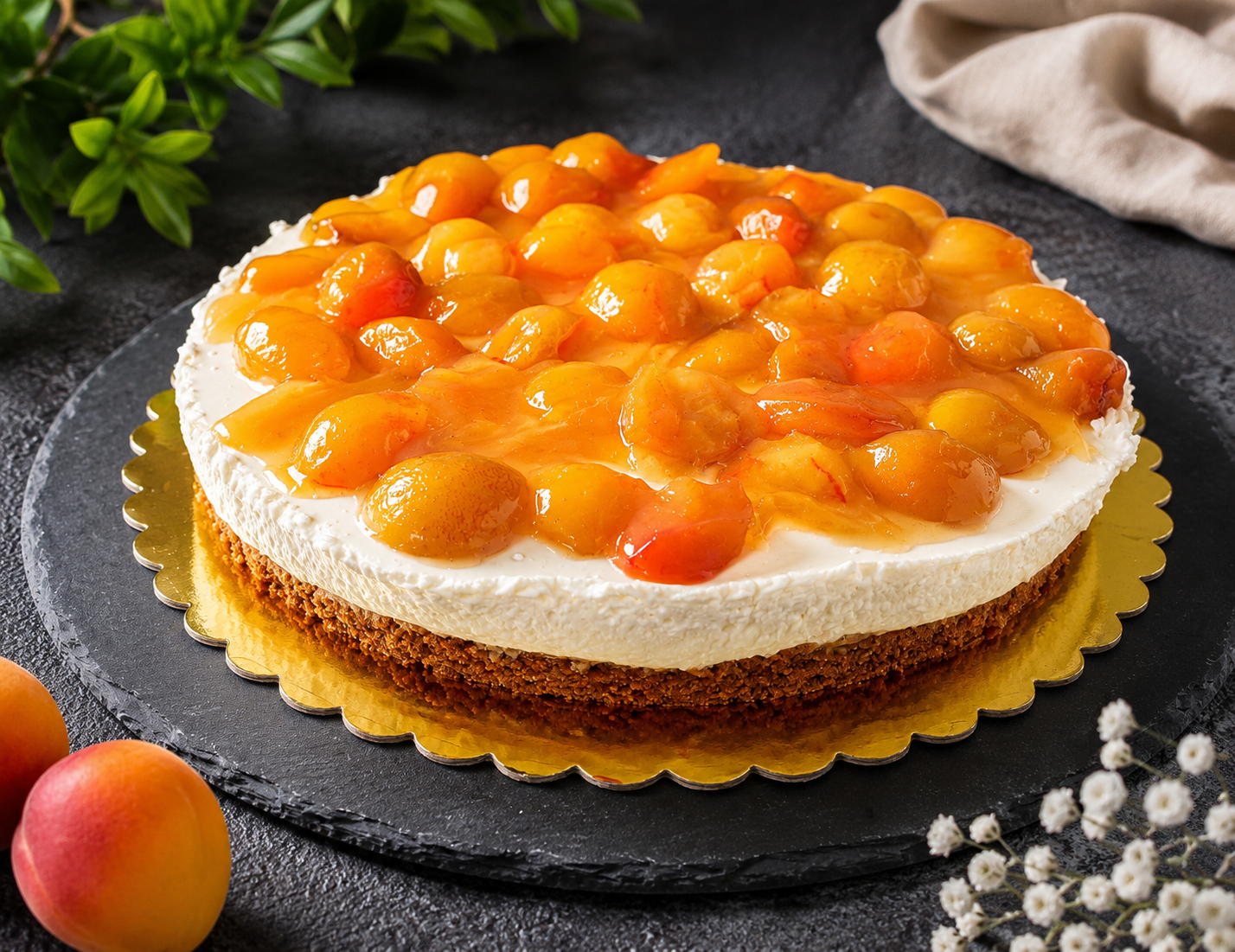 Gâteau au fromage nappé de mirabelles brillantes sur fond sombre, assiette dorée et feuilles vertes en arrière-plan.