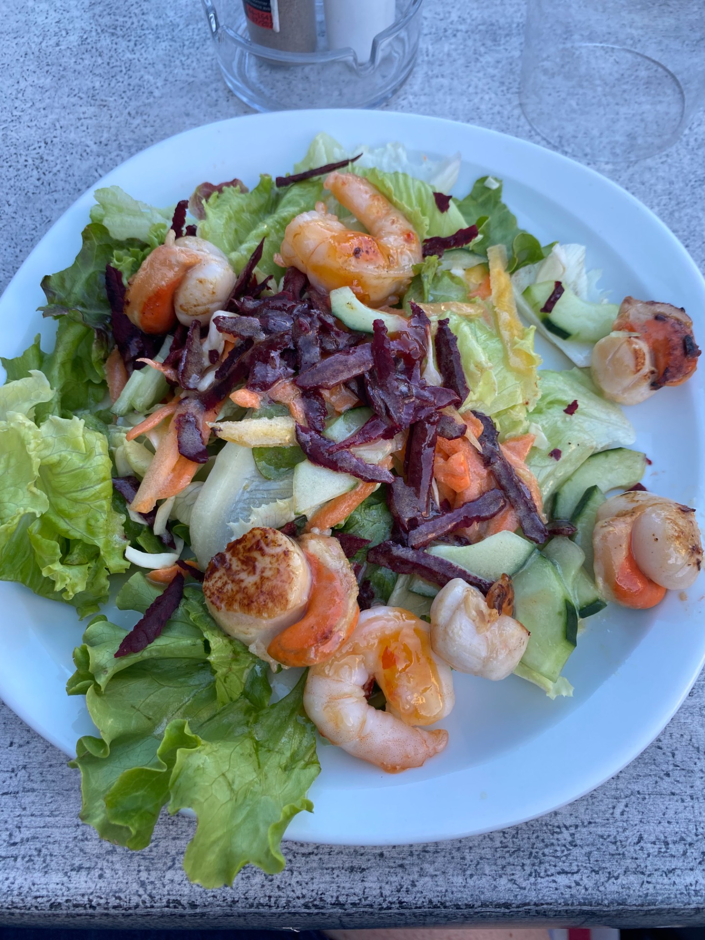 Assiette de salade verte avec crevettes grillées, concombres, carottes, betterave et morceaux de chou rouge.