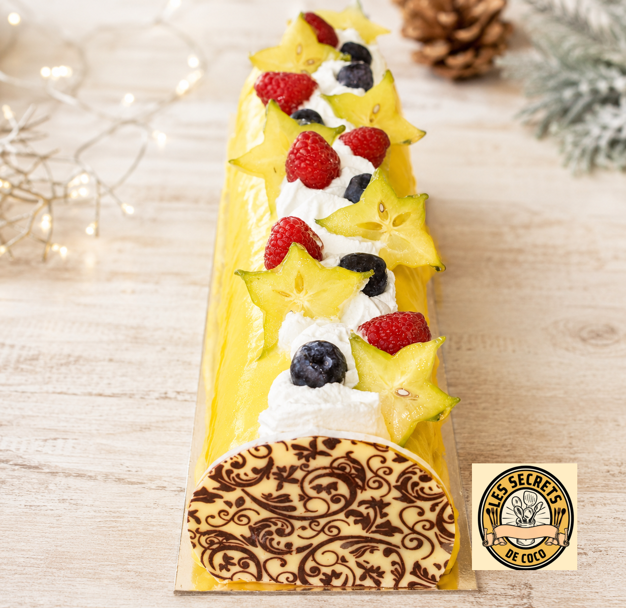 Bûche au citron jaune décorée de crème, fraises, framboises, myrtilles et logo Les Secrets de Coco.