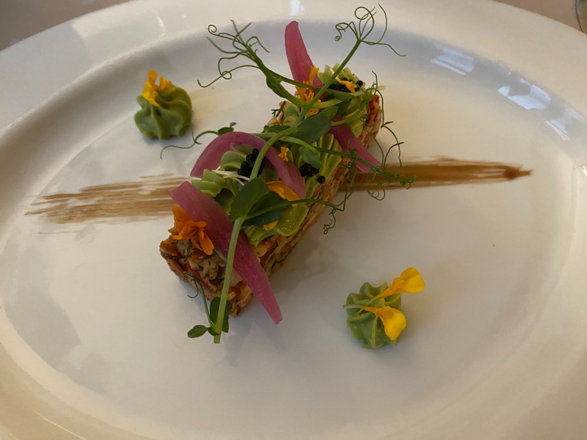 Assiette blanche avec bouquet de légumes verts, fleurs jaunes et rubans roses, décorations fines et herbes.
