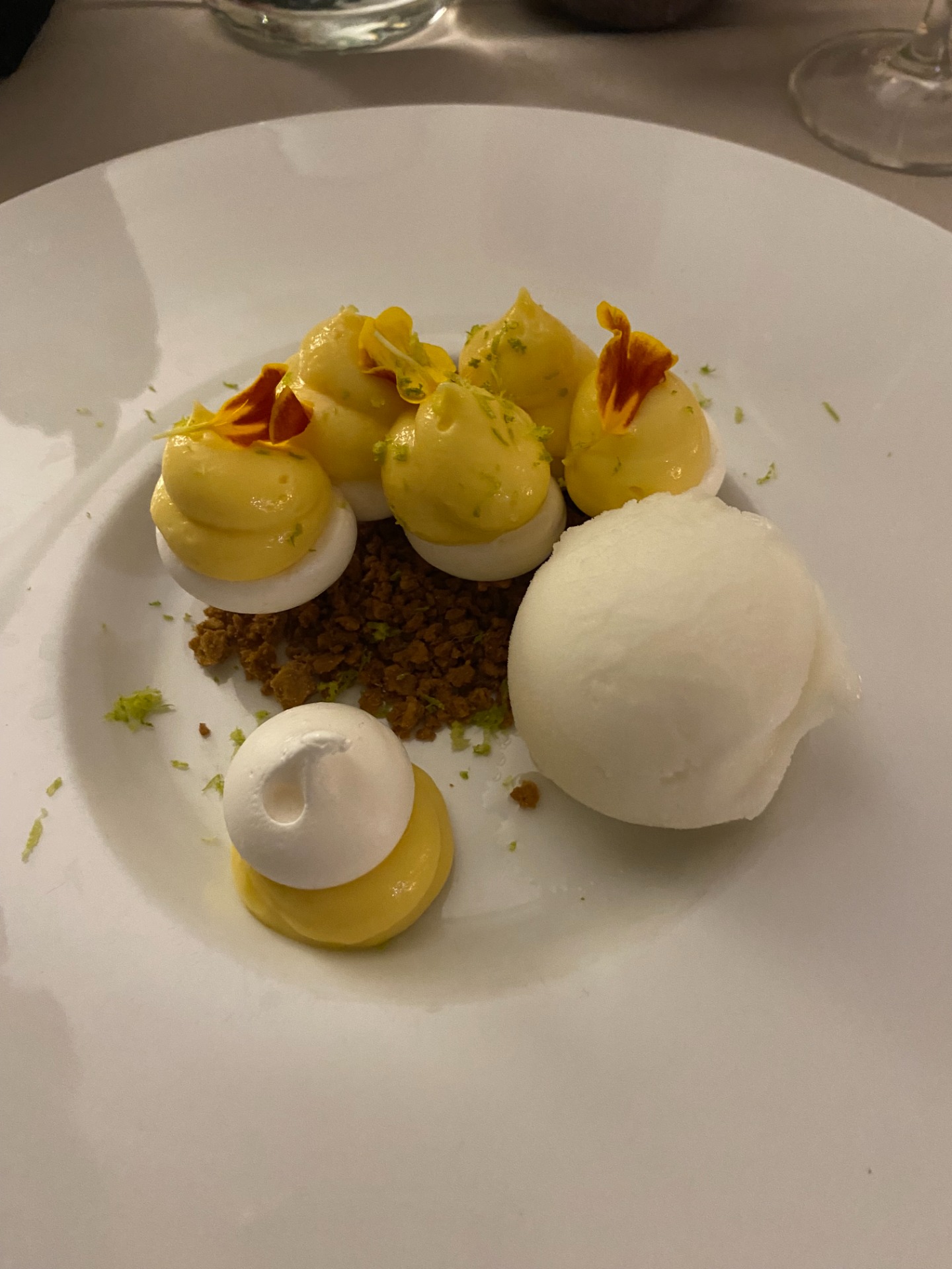 tarte au citron destructurée jaunes citron et blancs, sur assiette blanche, herbes et miettes d’épices.