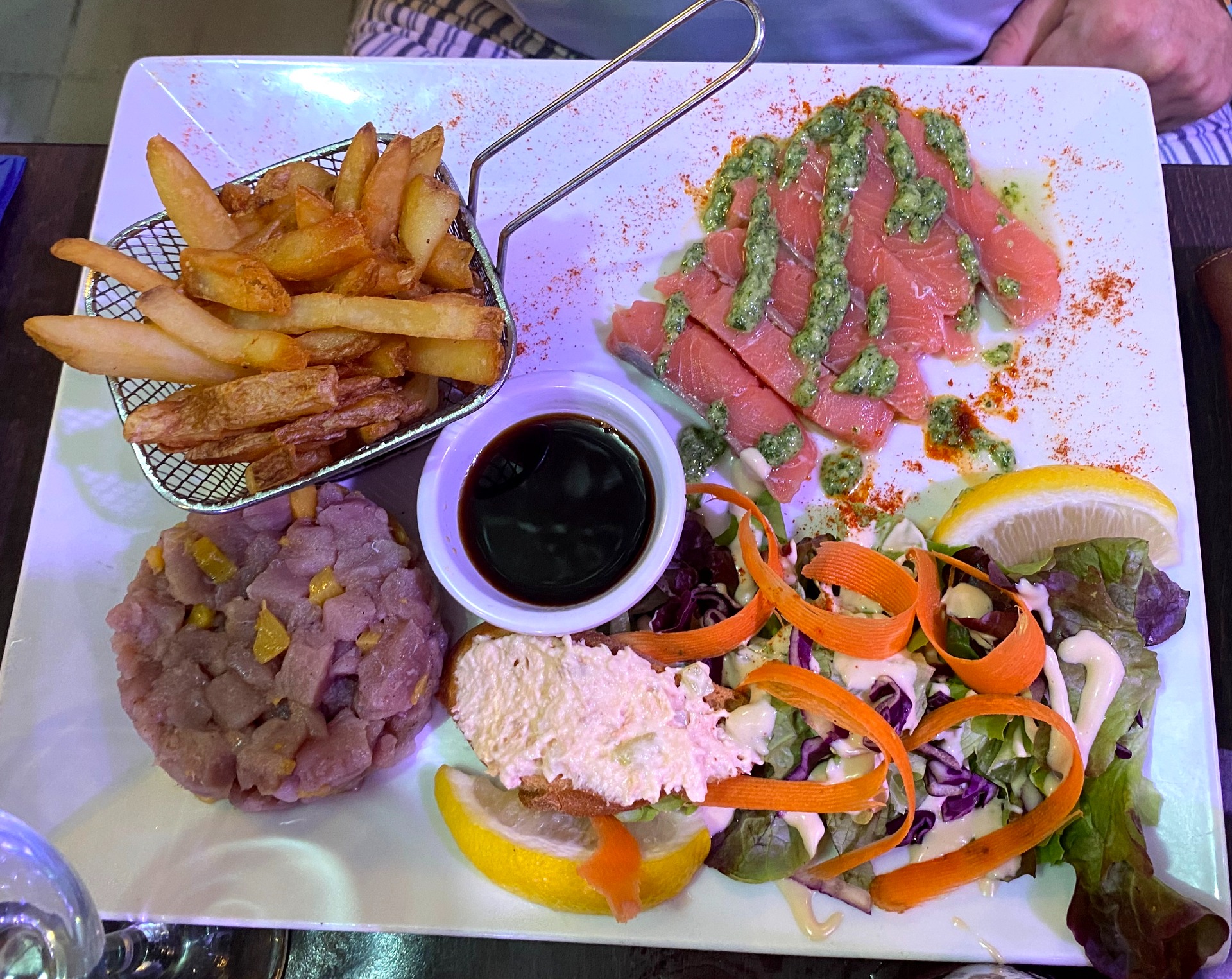 Assiette de poisson et salade, frites dorées, sauce noire, rondelles de citron et légumes croquants. carpaccio