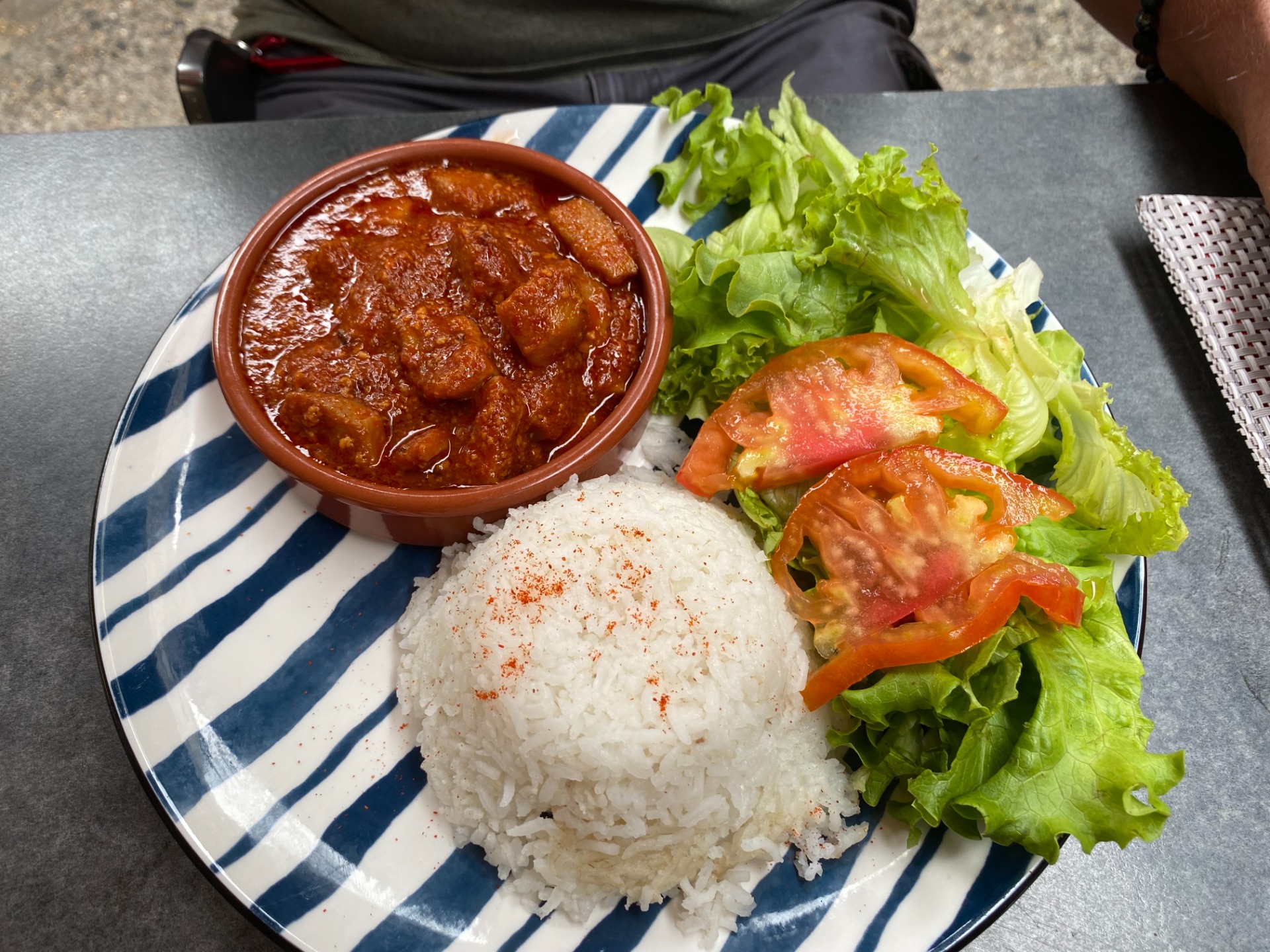 Assiette avec riz blanc, salade verte, tomates, et sauce brune épaisse dans un bol en terre cuite. seiche