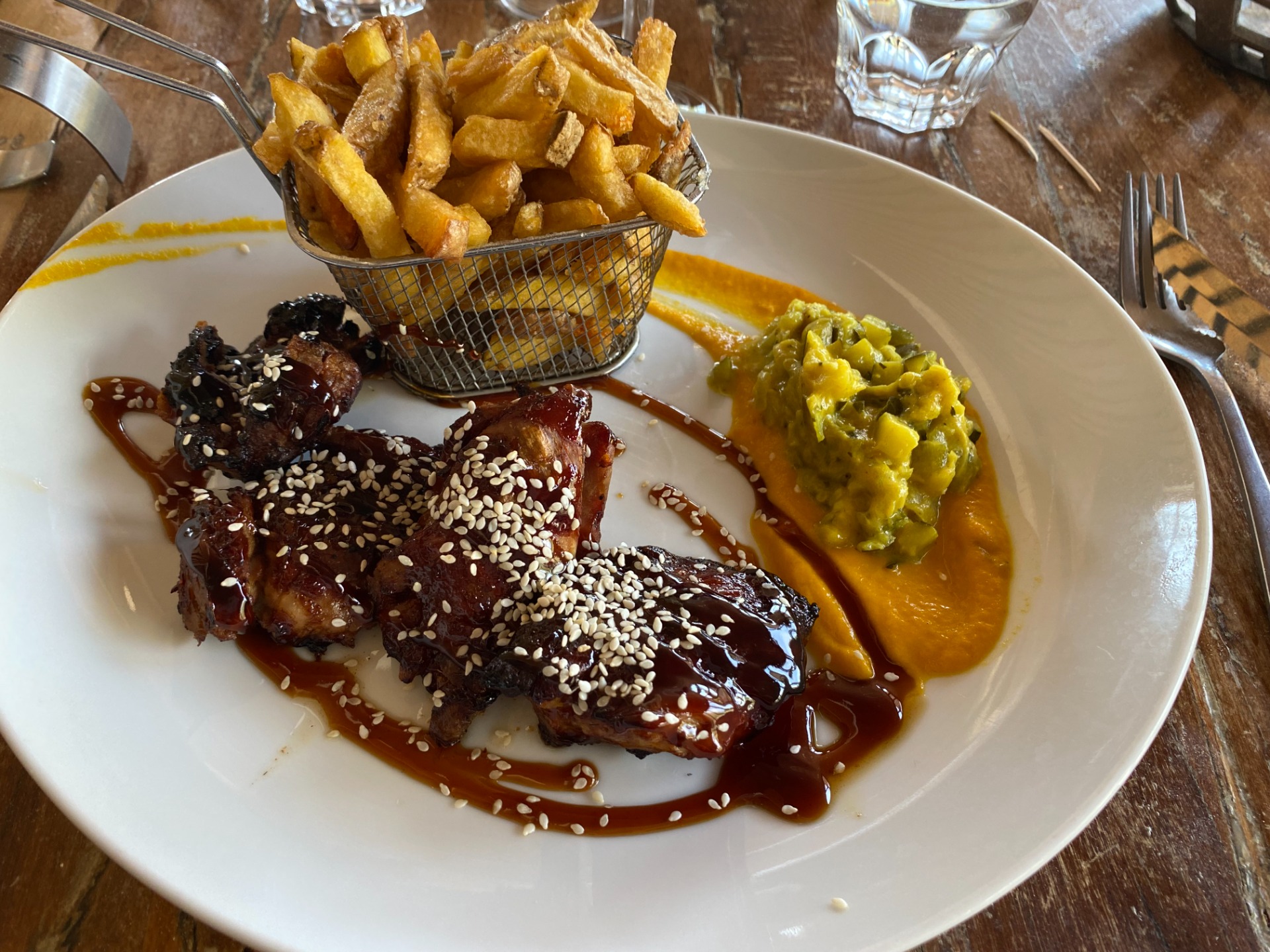 Assiette avec côtes de porc laquées au sésame, purée verte, sauce brune et frites en panier.