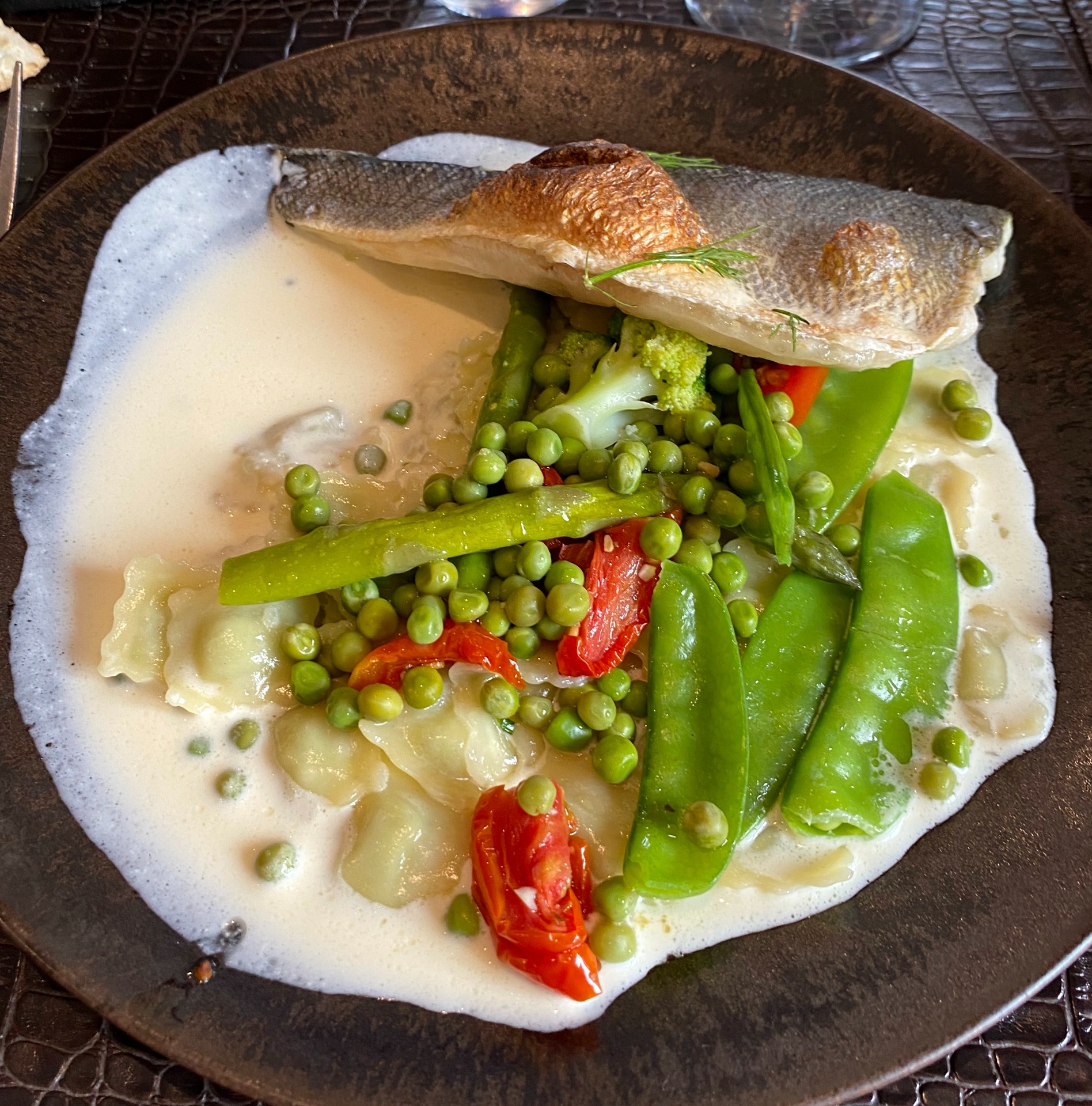 Assiette avec filet de poisson, légumes verts, pois, asperges et tomates, sur sauce blanche.