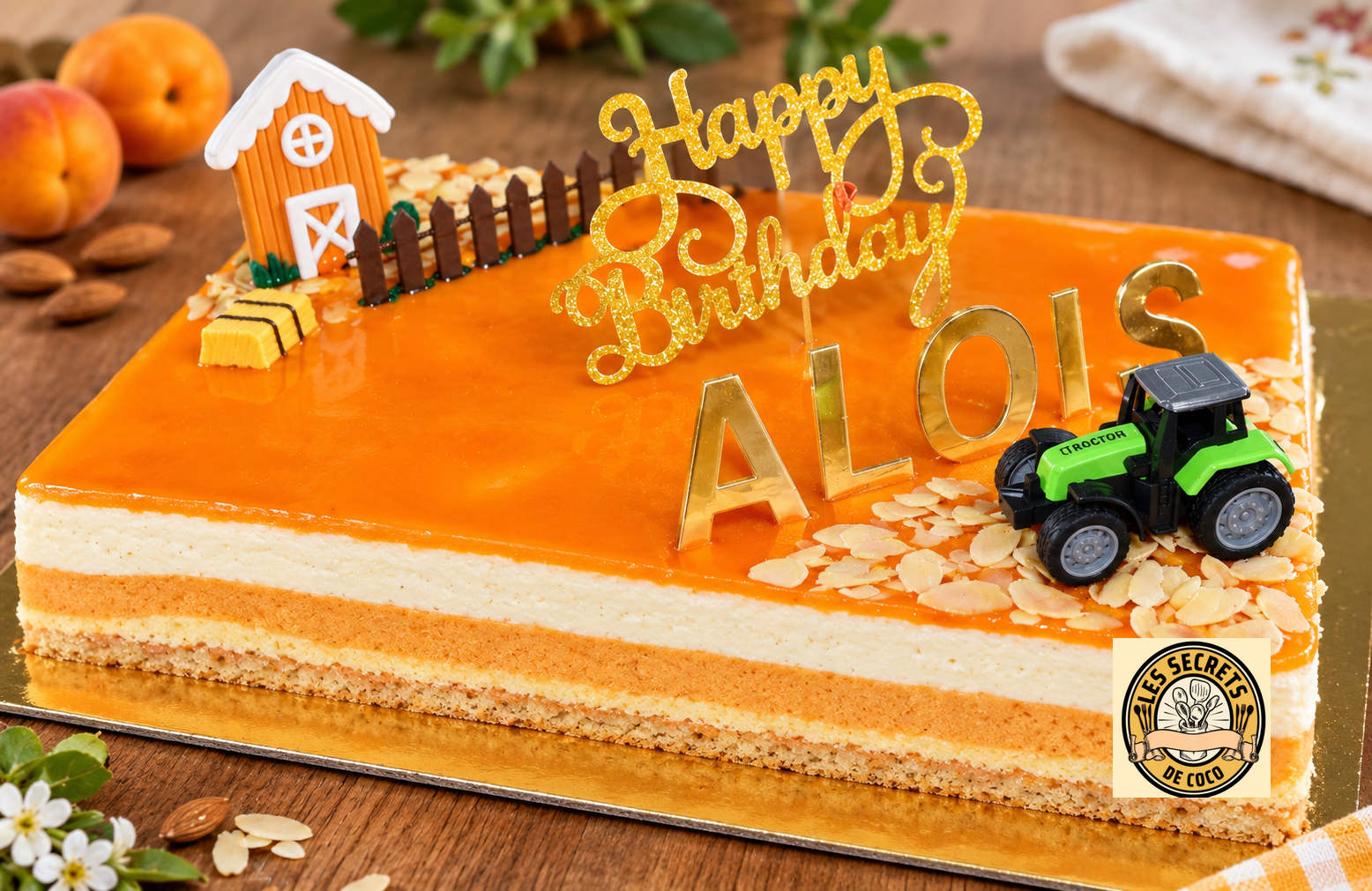 Gâteau orange à l abricot  (bavarois abricot amande) décoré, lettres dorées « Joyeux anniversaire », maison en chocolat, tracteur jouet vert et confettis.
