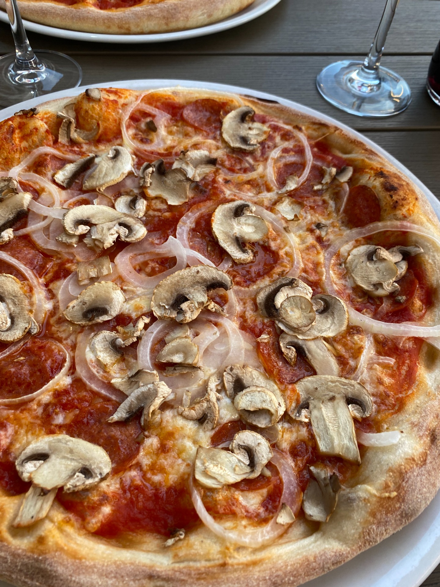 Pizza aux champignons et oignons, pâte croustillante, servie sur assiette blanche, verres à vin en arrière-plan.