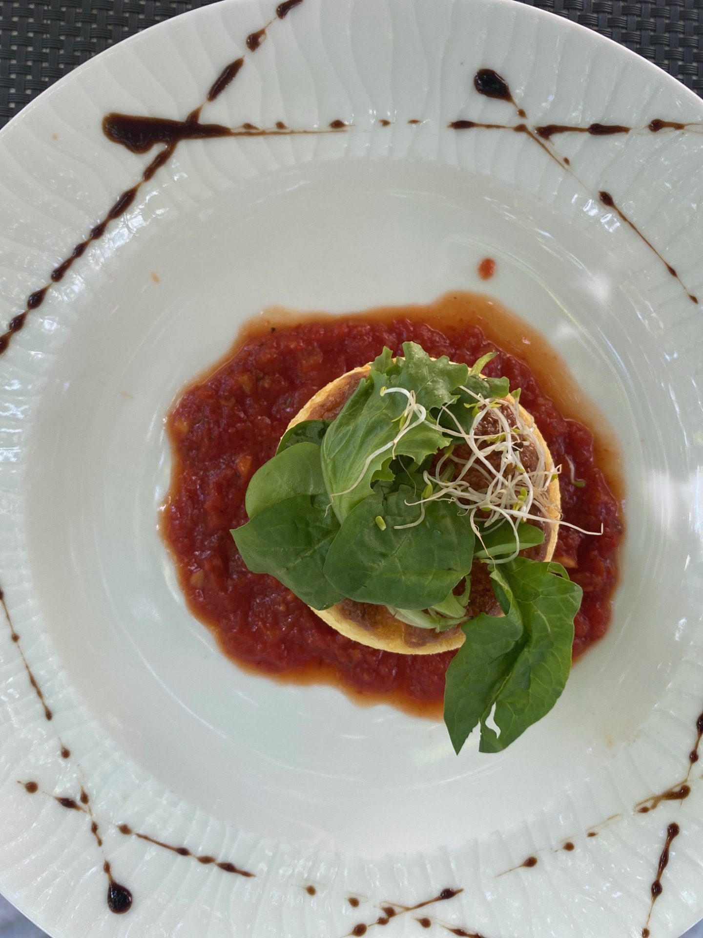 Assiette blanche avec sauce tomate rouge, escalope garnie de feuilles vertes et pousses germées, traces de balsamique.
