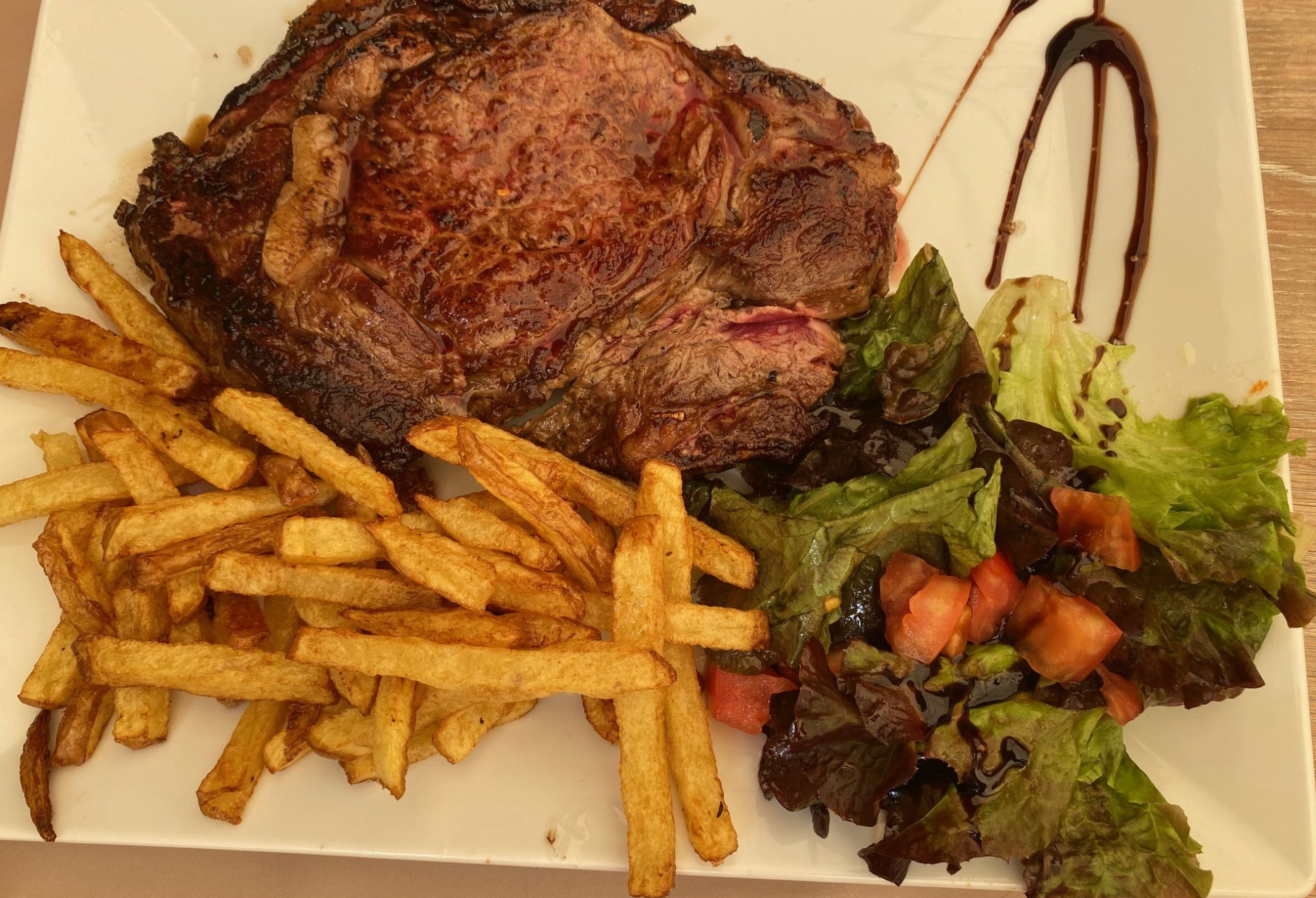 Assiette avec steak grillé, frites dorées, salade verte et tomates, nappées de sauce brune.